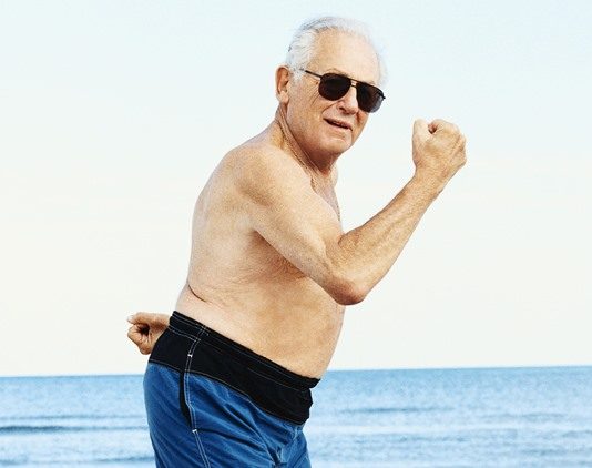 glad ældre mand i badebukser flekser muskler